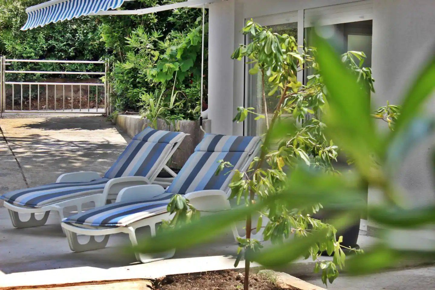 Garden terrace of the Apartment with two striped sun loungers under an awning