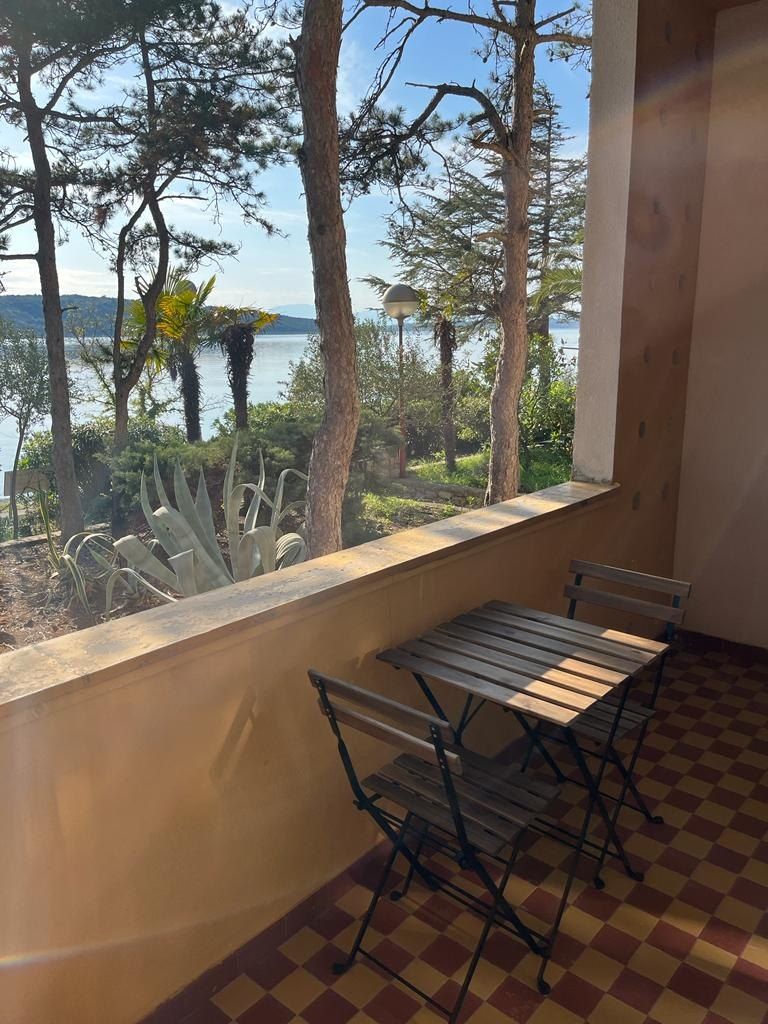 Balcony with a small table and two chairs, looking through pine trees to the sea